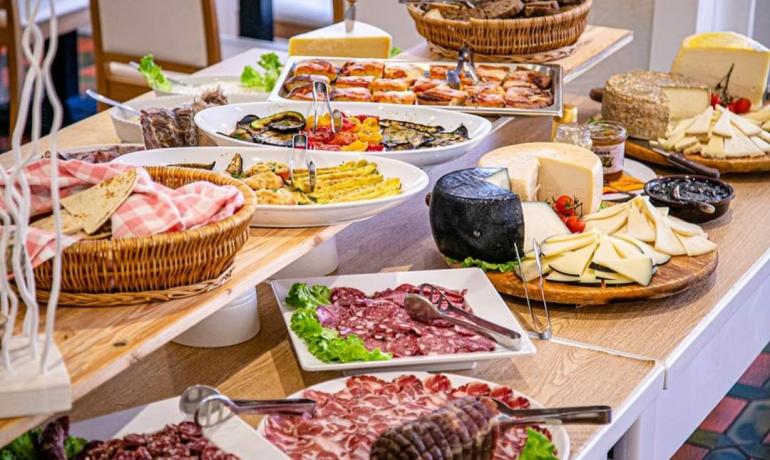 Buffet con formaggi, salumi e verdure grigliate su tavola di legno.
