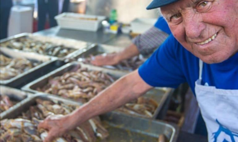 Uomo sorridente prepara pesce in un mercato affollato.